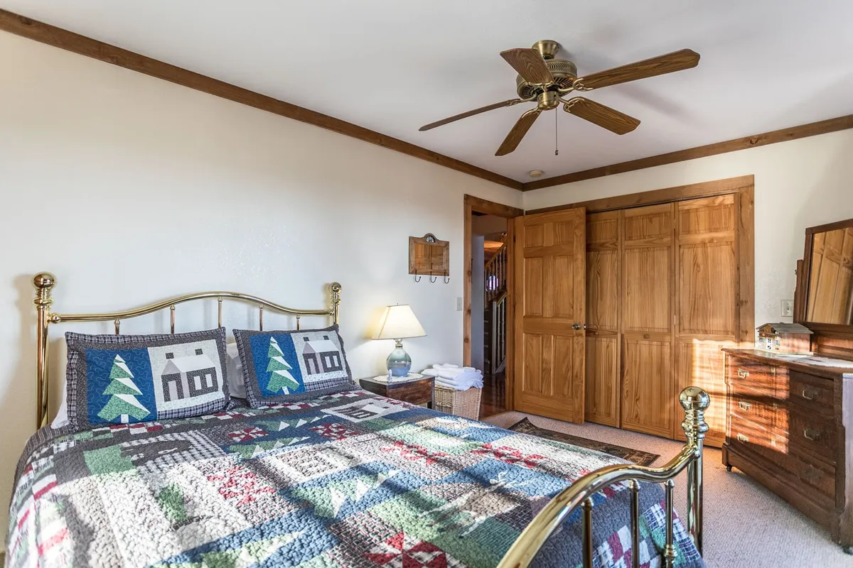 A cozy bedroom featuring a patterned quilt on the bed, wooden furniture, a ceiling fan, and a warm lamp. The inviting space suggests a comfortable spot for reading, relaxing, or unwinding after a day of adventure.