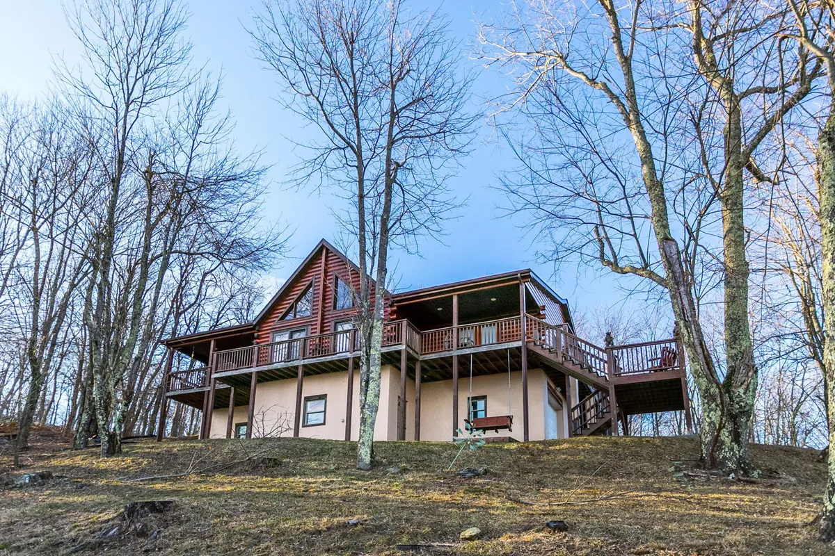 A wide view of the wooden deck nestled among tall trees, with the characteristic sloping roof of the cabin visible and natural light filtering through the greenery. The deck offers ample space for kids to play or for families to enjoy a meal outdoors, with the tranquil setting of the surrounding forest adding to the sense of retreat.