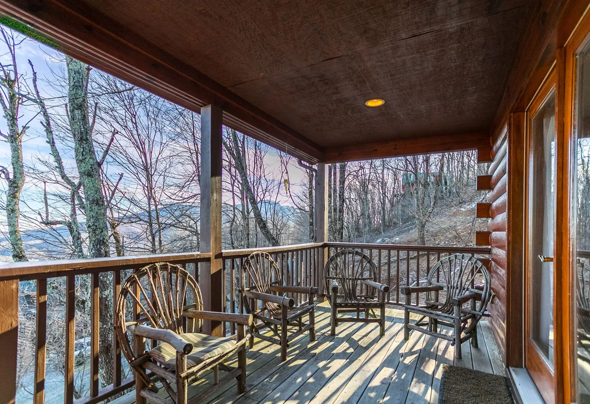 A serene exterior shot of a deck lined with classic wooden rocking chairs, facing out toward a stunning mountain view. The surrounding trees and open railing invite guests to relax with a book, sip coffee, or socialize while being immersed in nature. The tranquil mood underlines the peaceful, restorative aspects of the property.