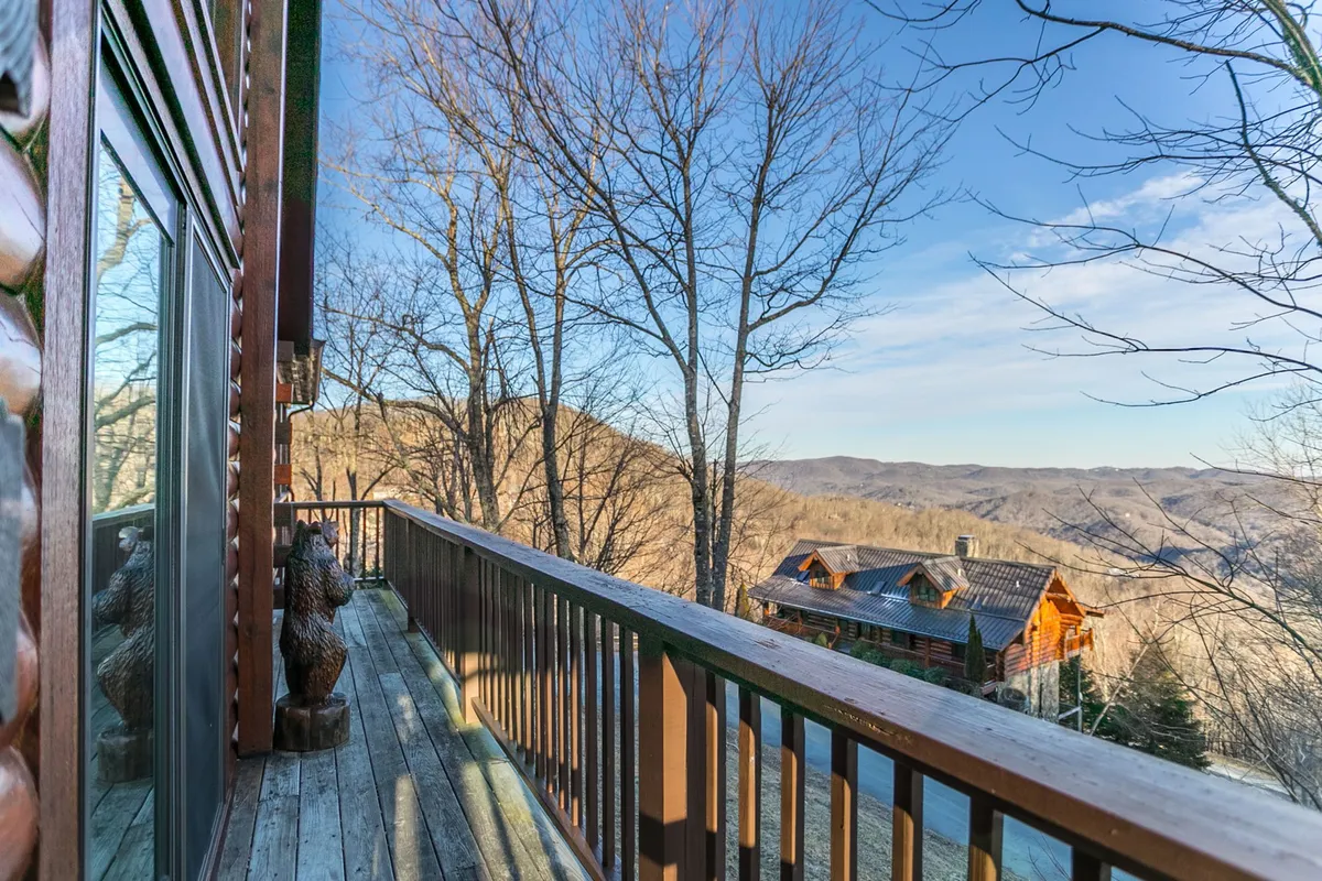 A tranquil exterior shot featuring a wooden balcony railing overlooking majestic mountain views and neighboring cabins, bordered by bare winter trees. This spot invites families to enjoy coffee in the morning or stargazing at night while soaking in the peacefulness of the mountains.
