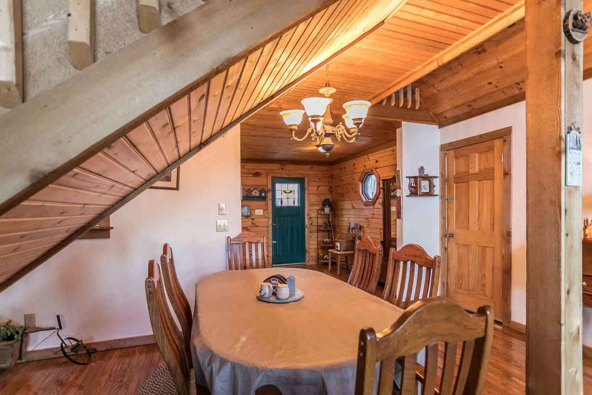 This photo highlights a large wooden dining table beneath a charming chandelier, with exposed wooden beams above and a colorful green door adding character. The table is set for gatherings, offering a cozy backdrop for shared meals and stories.