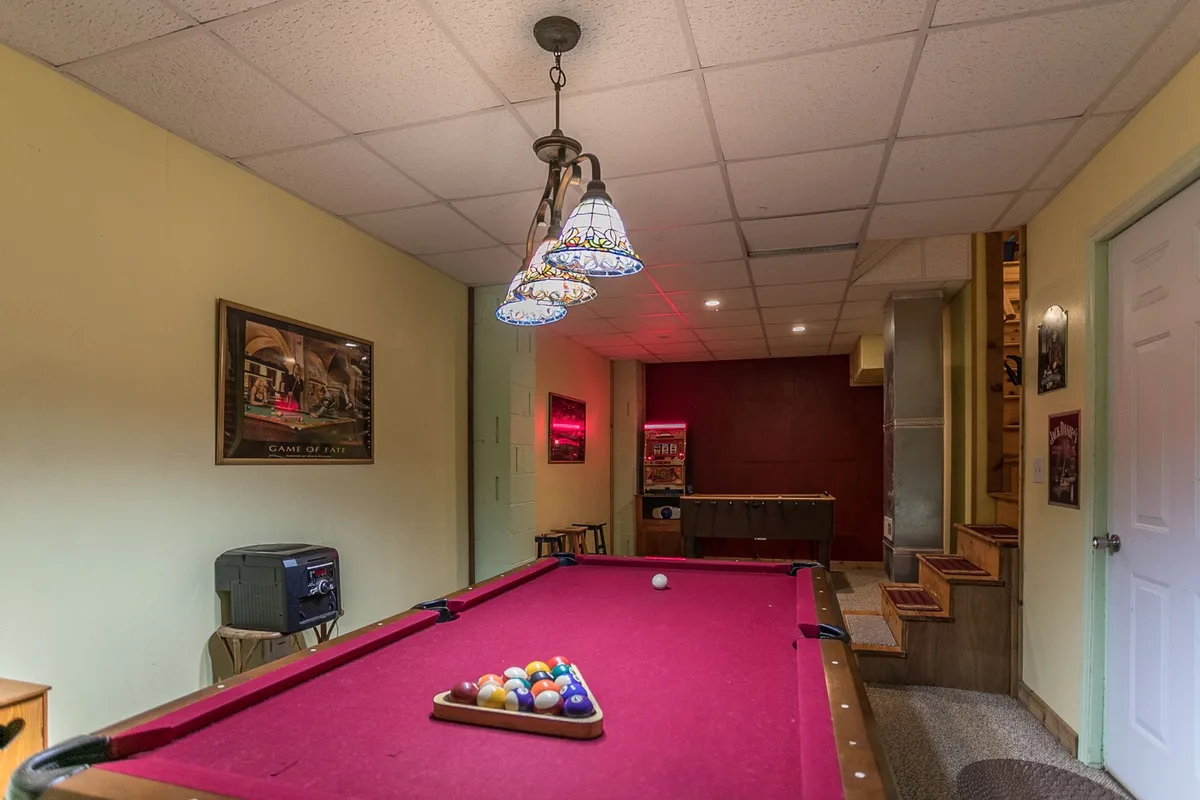 This image captures a vibrant game room featuring a pool table beneath a stained glass light fixture, a cozy bar area for refreshments, and playful wall decorations that enhance the lively atmosphere. The room is arranged for easy socializing and fun, inviting groups to gather for friendly competition.